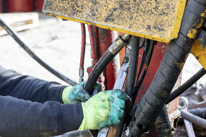 Worker is repairing hydraulic pipes of working machine. Hydraulic machines use liquid fluid power to perform work. Heavy construction vehicles are a common example.